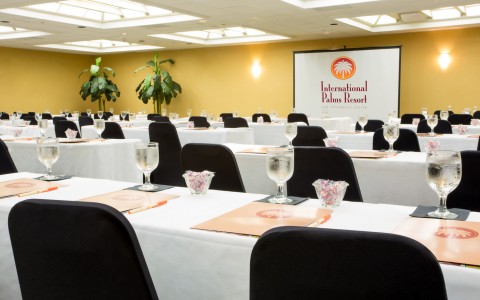 Meeting room with projection screen, rows of tables set with folders & glasses of water  