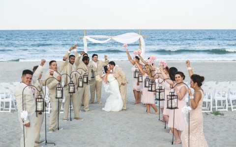 Bride and groom kissing in between bridesmaids and groomsmen on the beach  