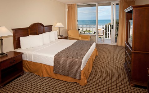 Room with king bed, wooden nightstands, dresser & balcony with ocean view 