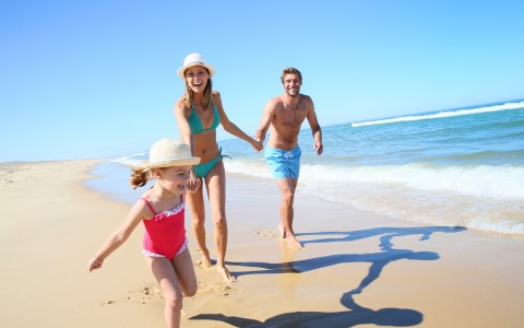 Couple with daughter running on the sand by the ocean water 